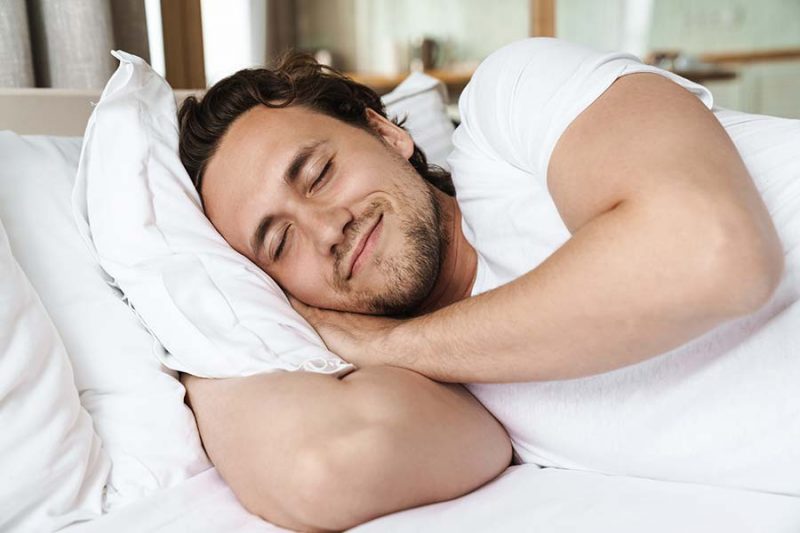 Man sleeping peacefully, resting in bed with a content smile.